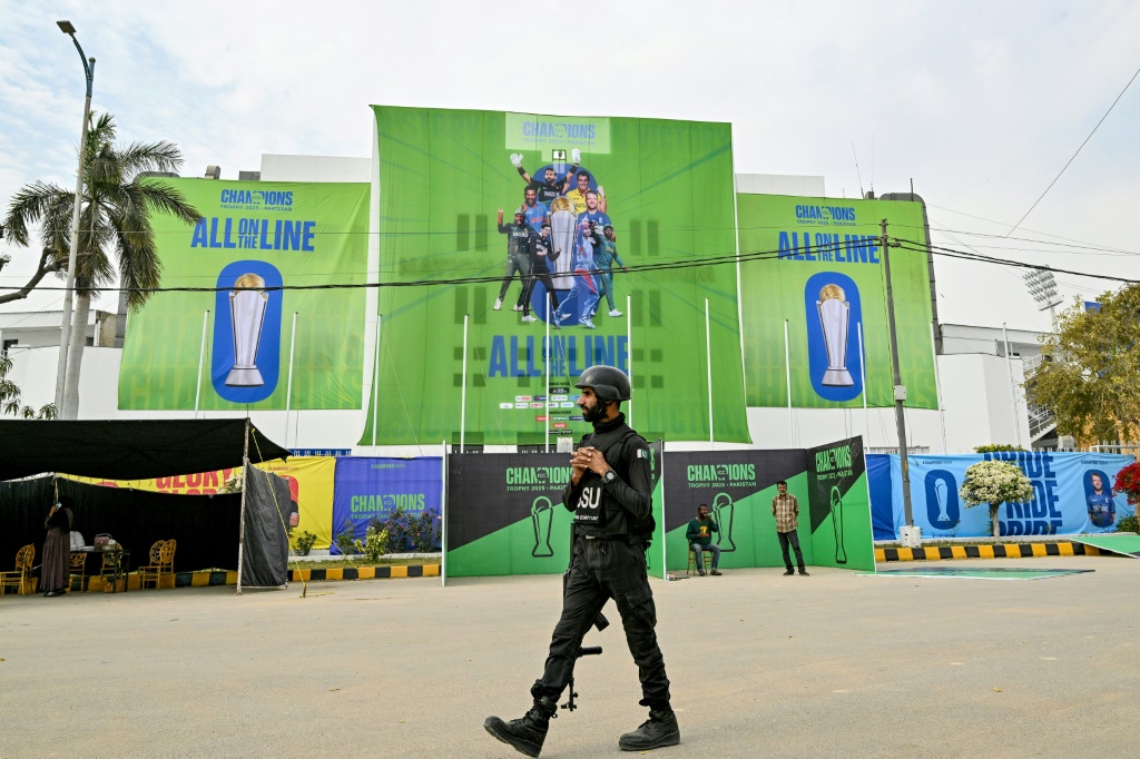 A Pakistani police commando walks past posters displayed ahead of the Champions Trophy in Karachi, AFP